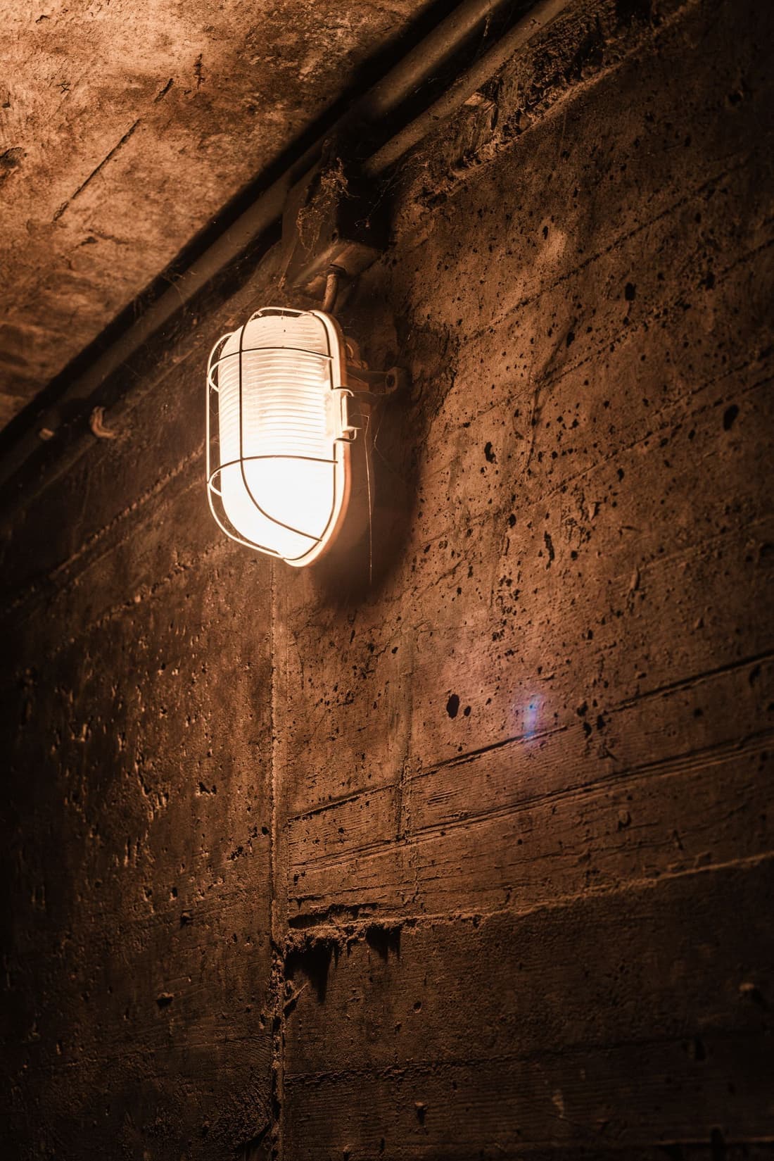 Basement concrete wall lit by a caged lamp