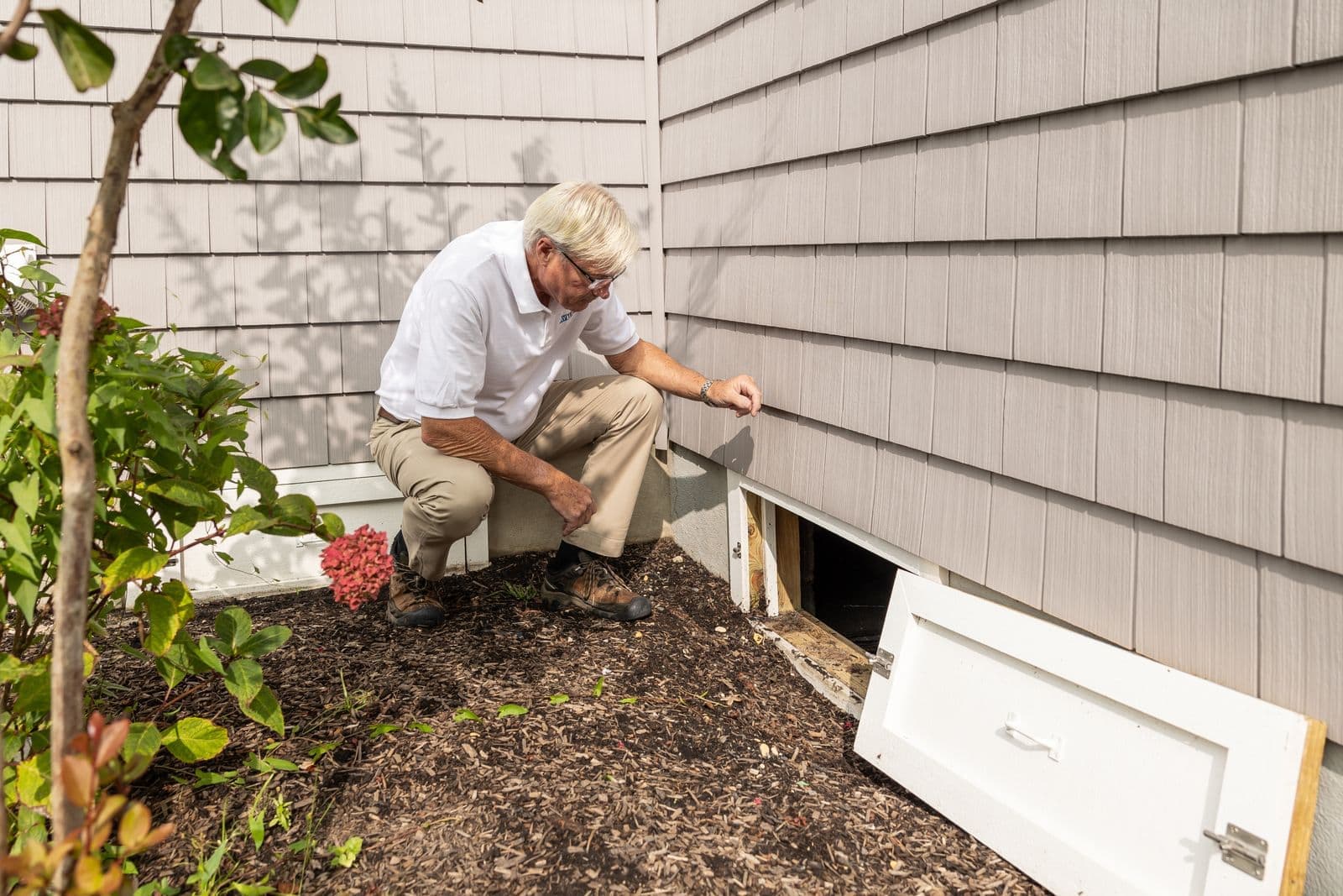 Inspector examining a crawl space opening outside a house
